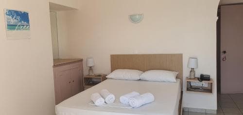 A cozy hotel room with a neatly made bed, rolled towels, and simple decor offers a comfortable stay for travelers seeking relaxation.