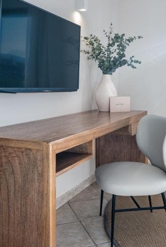 A cozy hotel room corner features a sleek wooden desk with a mounted TV above, a vase of fresh greenery, and a modern chair, creating an inviting workspace perfect for travelers seeking comfort and functionality.