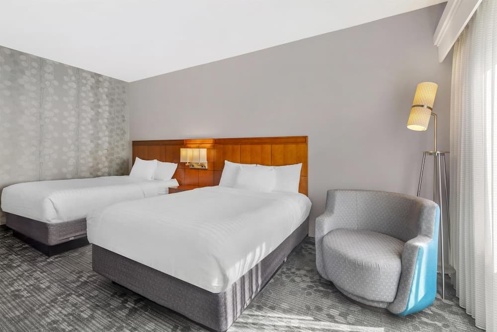 A cozy hotel room features two neatly made beds with white linens, a stylish armchair, and soft lighting, creating a serene atmosphere ideal for travelers seeking comfort and relaxation.