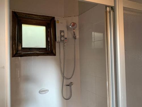 A compact bathroom with a tiled shower area, a mounted handheld showerhead, a wooden-framed mirror, and a frosted window offers a functional and private space ideal for travelers seeking basic amenities in a hotel or guesthouse setting.