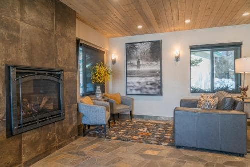 A cozy living room with a stone fireplace, plush seating, and large windows overlooking snowy scenery offers a serene retreat ideal for winter getaways.