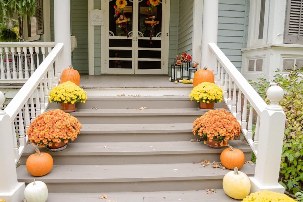 A charming front porch adorned with vibrant autumn flowers, pumpkins, and festive decorations creates a welcoming seasonal atmosphere perfect for fall-themed travel photography.