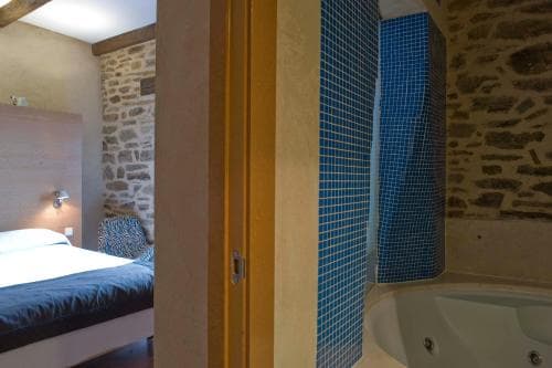 A cozy bedroom with rustic stone walls transitions into a serene bathroom featuring blue mosaic tiles and a luxurious bathtub, ideal for travelers seeking relaxation in a charming retreat.