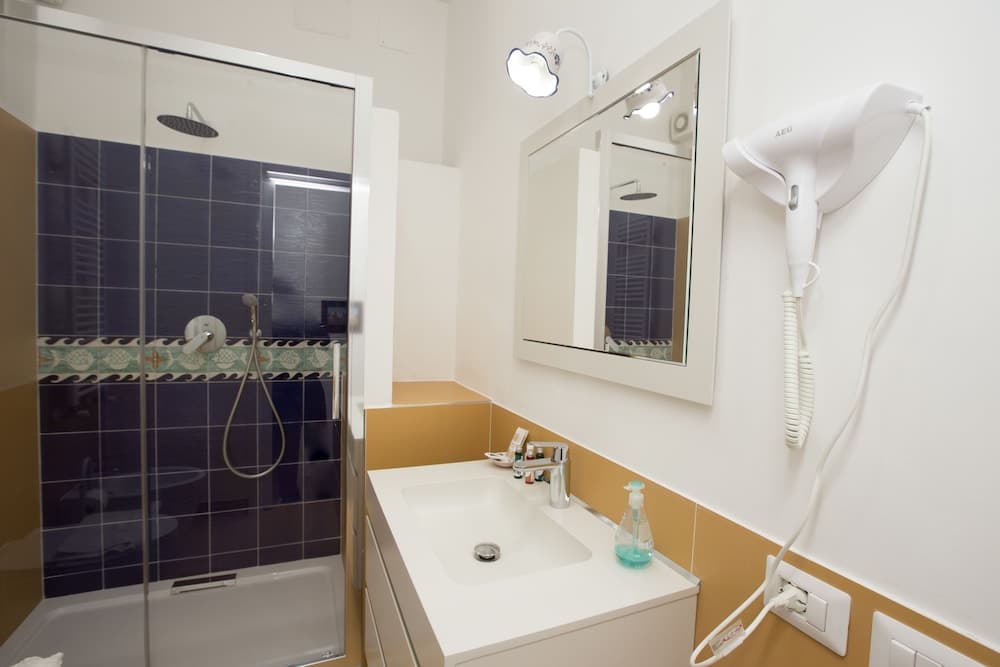 A cozy hotel bathroom features a modern shower with blue tiles, a sleek white sink, a mounted hairdryer, and warm lighting, ideal for travelers seeking comfort and convenience.