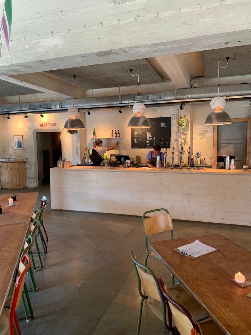 A cozy industrial-style café with wooden tables, colorful chairs, and exposed concrete ceilings offers a relaxed dining atmosphere in Henningsvær, Norway, perfect for travelers seeking a unique dining experience.