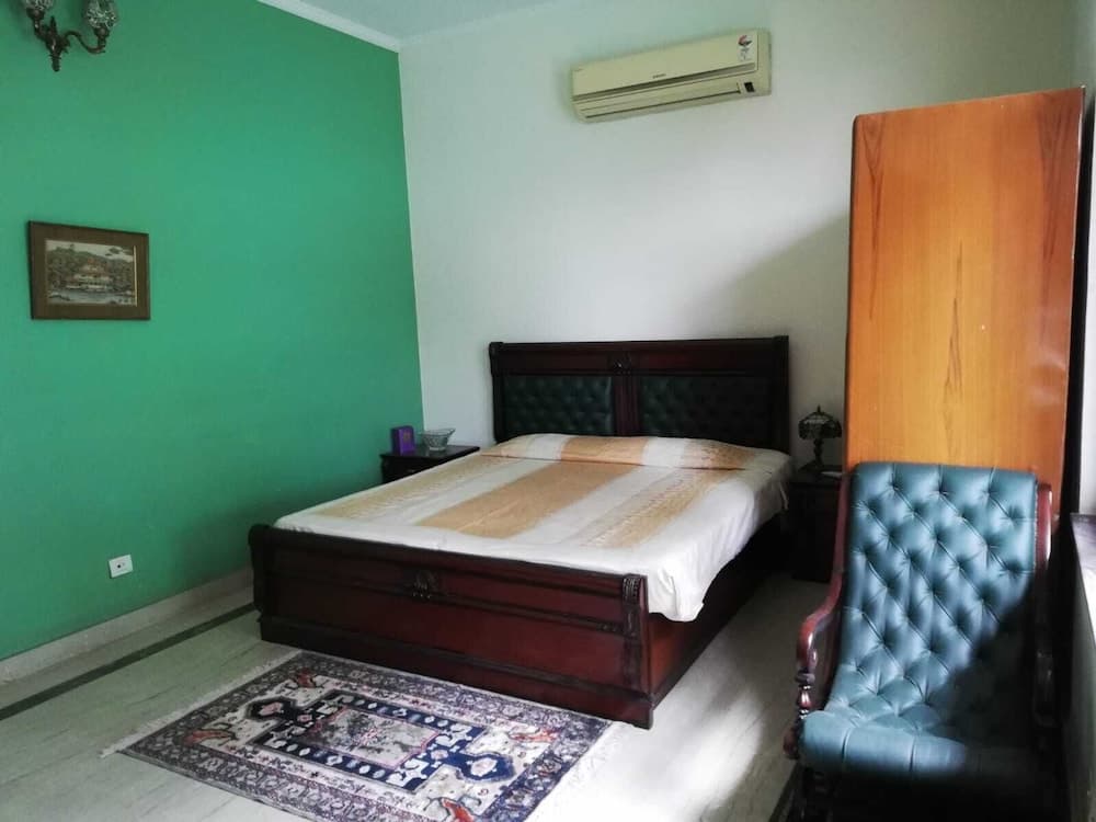 A cozy bedroom with a green accent wall, wooden bed, patterned rug, and leather chair offers a serene retreat for travelers seeking comfort and relaxation.