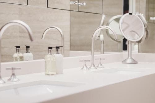 A modern bathroom vanity with sleek faucets, neatly arranged toiletries, and a magnifying mirror reflects a clean and minimalist aesthetic, ideal for travelers seeking upscale accommodations.