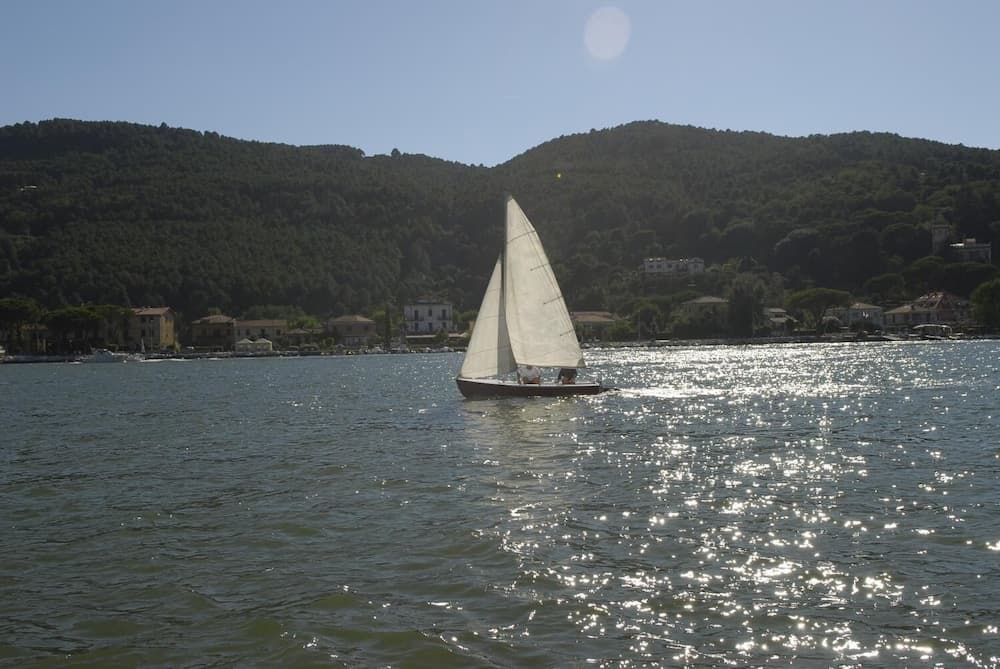 A serene sailboat glides across a sparkling lake surrounded by lush green hills and quaint houses, ideal for tranquil boating adventures and scenic photography.