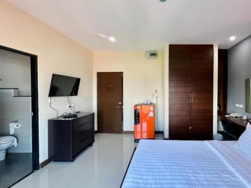 A cozy hotel room features a neatly made bed, a small orange refrigerator, a flat-screen TV on a dresser, and an open bathroom door, ideal for travelers seeking comfort and convenience in a compact space.