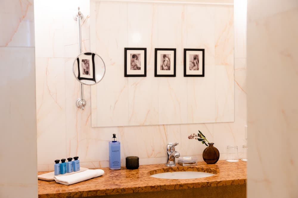 A luxurious hotel bathroom features a marble countertop adorned with neatly arranged toiletries, framed artwork on the wall, and a cozy ambiance ideal for travelers seeking comfort and elegance.