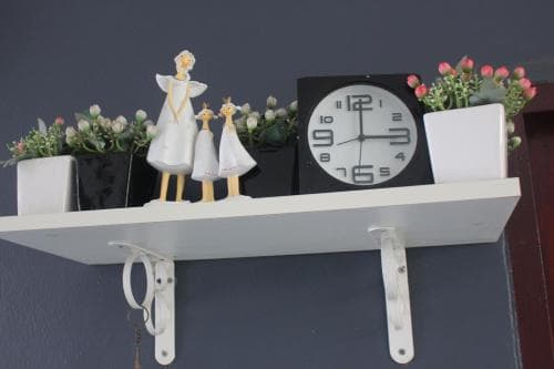 A cozy indoor shelf adorned with angel figurines, potted plants, and a modern clock creates a serene atmosphere, perfect for travelers seeking a peaceful home away from home.