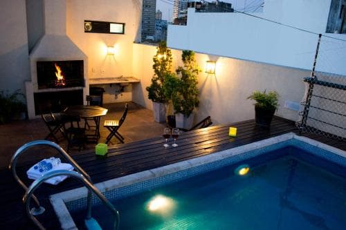 A cozy rooftop patio features a glowing pool, outdoor fireplace, and intimate seating area, perfect for a romantic evening getaway in an urban setting.
