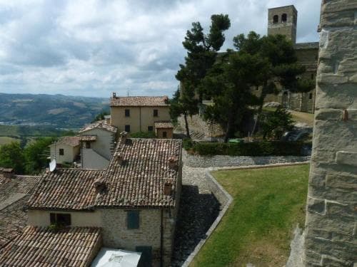 A serene medieval village scene with stone buildings, terracotta roofs, lush greenery, and distant hills under a partly cloudy sky, ideal for cultural heritage tourism and photography enthusiasts.