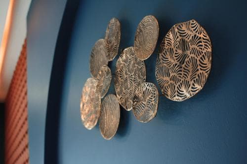 A serene indoor setting features an artistic arrangement of metallic, leaf-patterned discs on a deep blue wall, ideal for travelers seeking modern decor inspiration for home or office spaces.