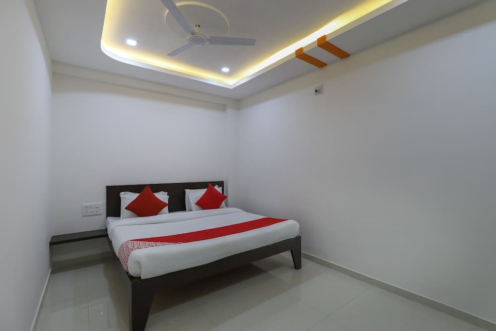 A cozy hotel room features a neatly made bed with red accents under soft ceiling lights, ideal for travelers seeking comfort and simplicity.