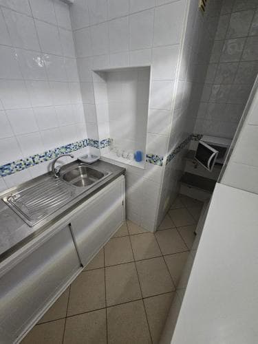 A compact kitchen with tiled walls, a stainless steel sink, and a microwave creates a functional and clean space ideal for travelers seeking self-catering accommodations.