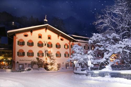 A cozy, snow-covered alpine hotel illuminated at night offers a serene winter retreat, perfect for travelers seeking a picturesque mountain getaway.