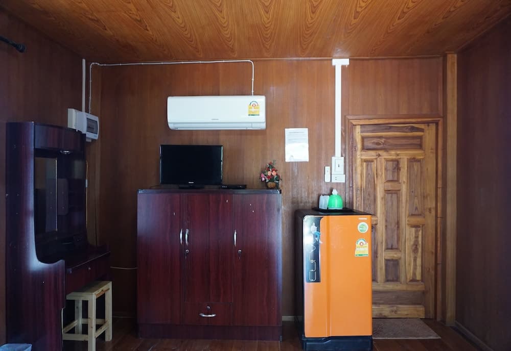 A cozy wooden cabin interior features a warm ambiance with a flat-screen TV atop a cabinet, an orange refrigerator, and a wooden door, ideal for travelers seeking a rustic retreat.