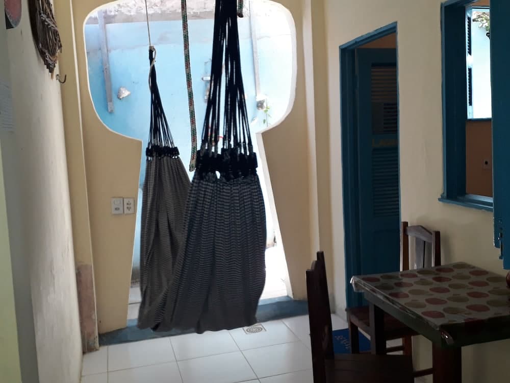 A cozy indoor space features hanging hammocks by an arched doorway, a tiled floor, and a table with chairs, creating a relaxed atmosphere ideal for travelers seeking comfort in a homely setting.