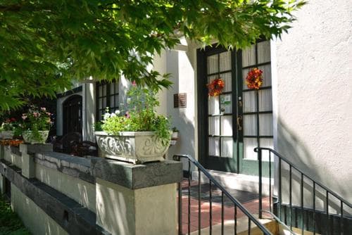 A charming white building entrance adorned with lush greenery, vibrant flower arrangements, and a welcoming staircase creates an inviting atmosphere ideal for boutique hotel stays or quaint city retreats.