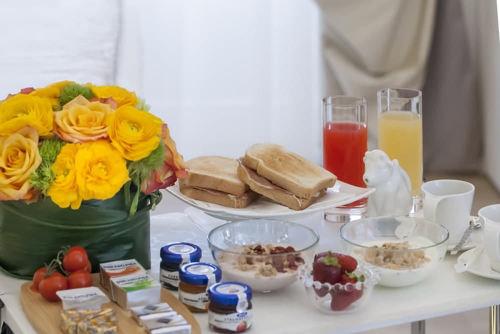 A cozy hotel breakfast setup features a vibrant bouquet of yellow flowers, assorted sandwiches, fresh juices, yogurt bowls, and condiments, creating an inviting and refreshing morning ambiance ideal for travelers seeking comfort and convenience.