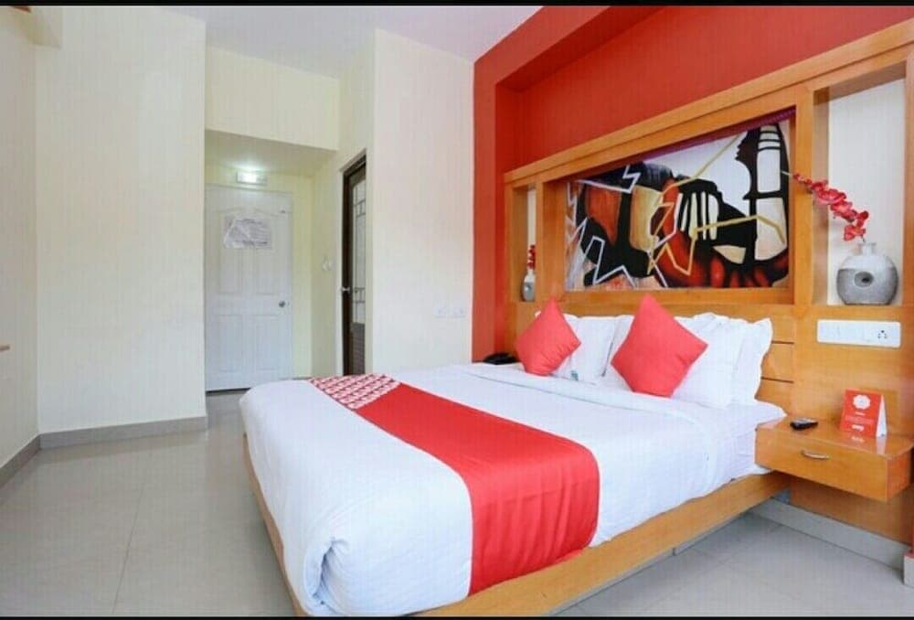 A cozy hotel room features a neatly made bed adorned with red accents, vibrant wall art, and modern furnishings, ideal for travelers seeking comfort and style during their stay.