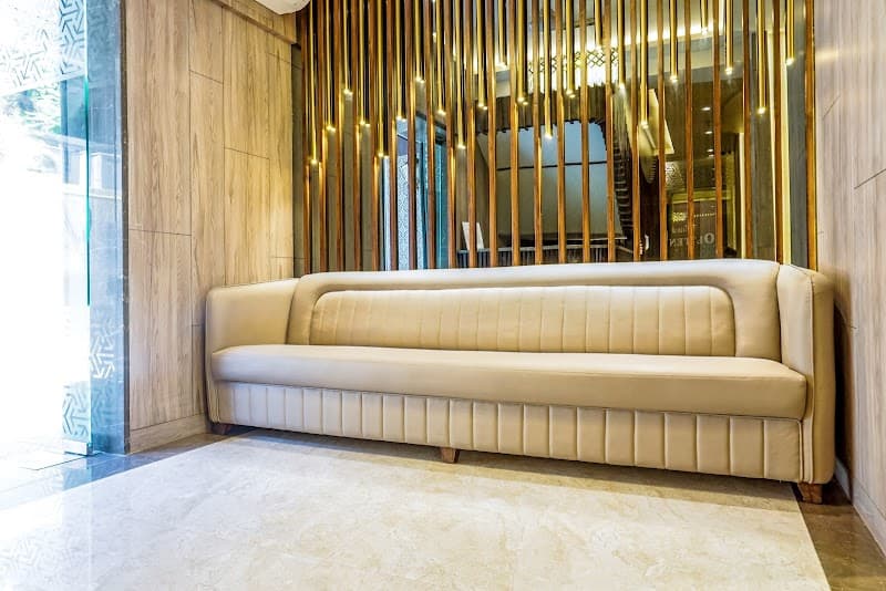 A cozy beige sofa sits invitingly against a modern wooden wall adorned with golden vertical lights, creating a warm and luxurious atmosphere in the lobby of Hotel Oltens, perfect for travelers seeking comfort and style in Mumbai.