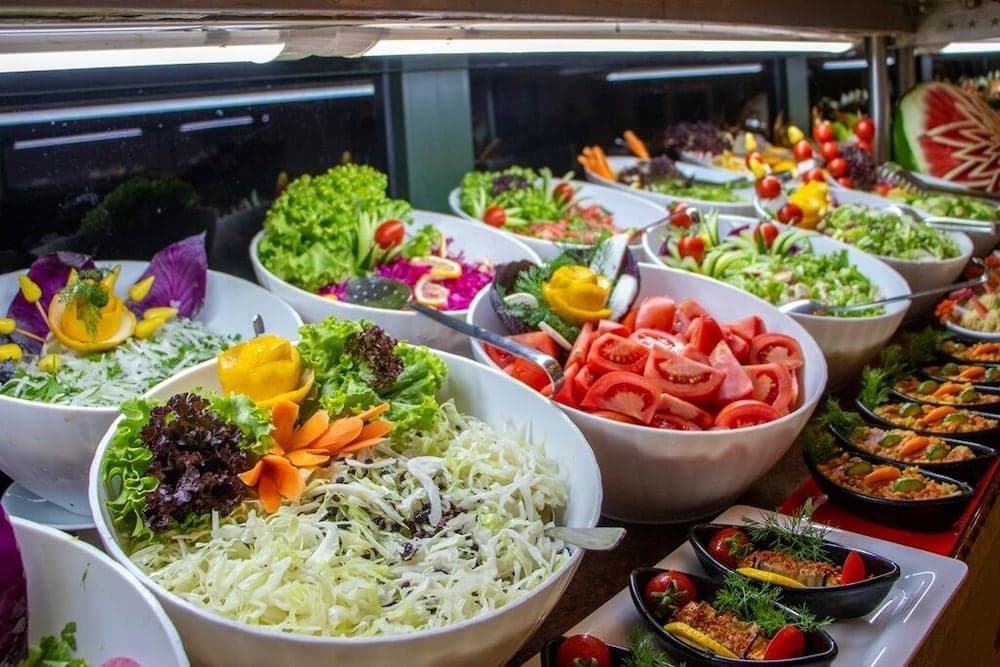 A vibrant buffet display featuring colorful salads and fresh vegetables in a well-lit indoor setting evokes a cheerful dining atmosphere, ideal for travelers seeking healthy meal options during their journey.