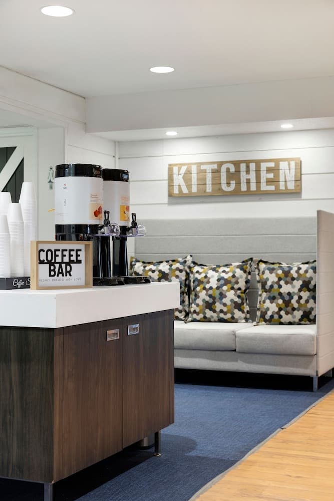 A cozy lounge area features a modern coffee bar with sleek dispensers and a plush sofa adorned with patterned cushions, ideal for travelers seeking a comfortable spot to relax and recharge.