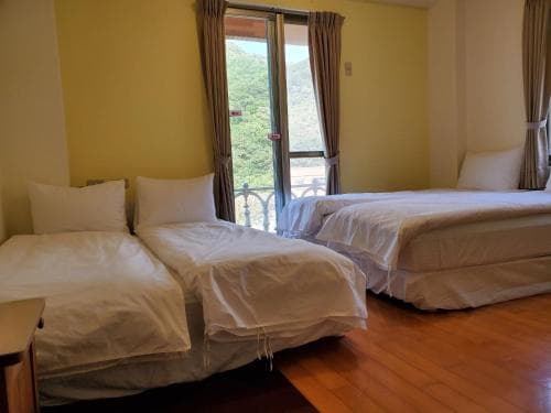 A cozy hotel room with two neatly made beds, wooden flooring, and a scenic view of greenery through a balcony window, ideal for travelers seeking comfort and relaxation.