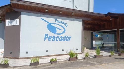 A welcoming Pousada Pescador entrance features a clean facade with blue branding, potted plants, and a modern design, ideal for travelers seeking a cozy seaside stay.