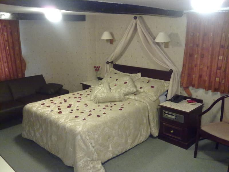 A cozy hotel room with a romantic ambiance features a bed adorned with rose petals under a canopy, warm curtains, and bedside lamps, ideal for a couples' getaway.