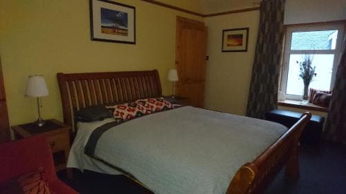 A cozy hotel room with a wooden sleigh bed, framed artwork on yellow walls, and a window view of snowy rooftops, ideal for travelers seeking comfort in a quaint setting.