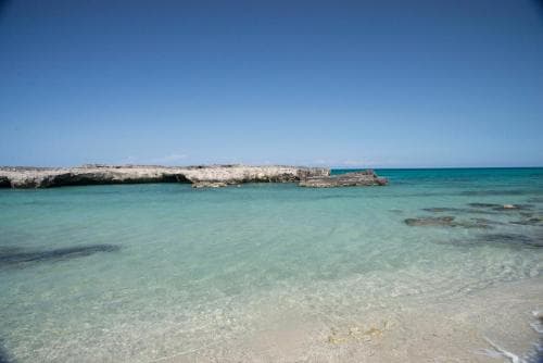 A serene tropical beach with crystal-clear turquoise waters, sandy shores, and rocky formations under a clear blue sky, ideal for relaxation and nature photography.
