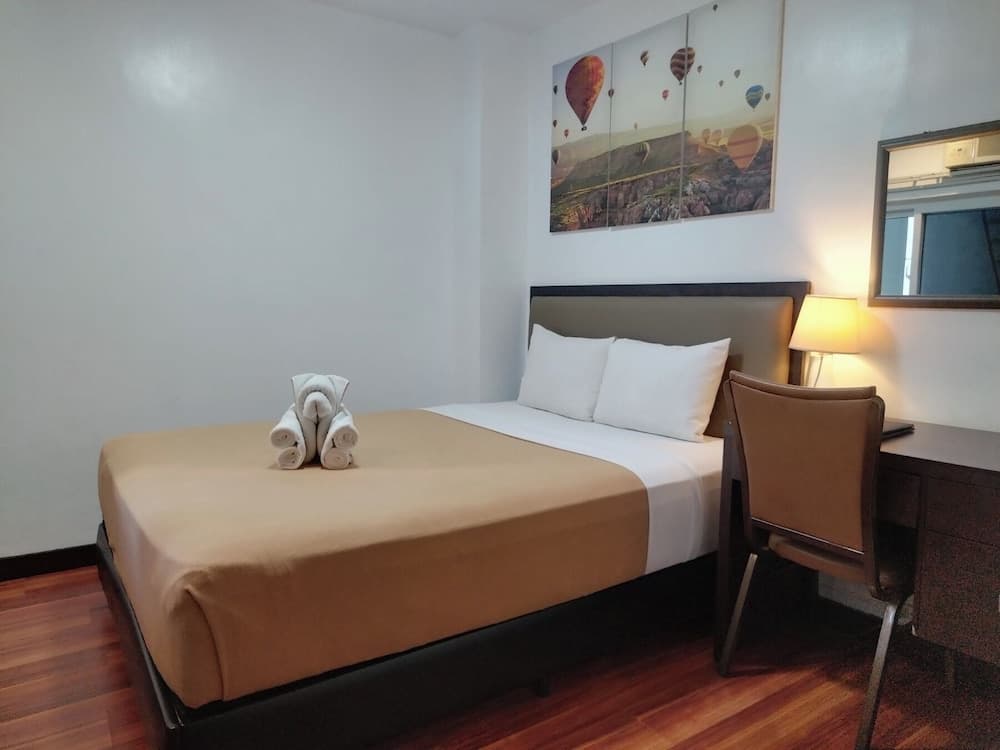A cozy hotel room features a neatly made bed adorned with towel animals, a desk with a chair, warm lighting from a bedside lamp, and a vibrant hot air balloon artwork, ideal for travelers seeking comfort and relaxation.