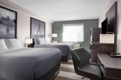 A cozy hotel room features two neatly made beds, modern artwork, a desk with a chair, and soft lighting, creating a serene atmosphere ideal for travelers seeking comfort and relaxation.