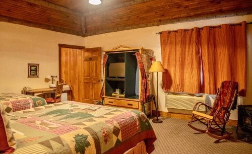A cozy cabin bedroom with warm wooden accents, a quilted bed, rocking chair by the window, and rustic decor invites travelers seeking a serene retreat in nature.