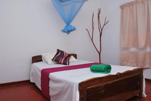 A cozy guesthouse room features a neatly made bed adorned with colorful linens, a decorative branch stand, and a mosquito net, evoking a warm and inviting atmosphere ideal for budget travelers seeking comfort.