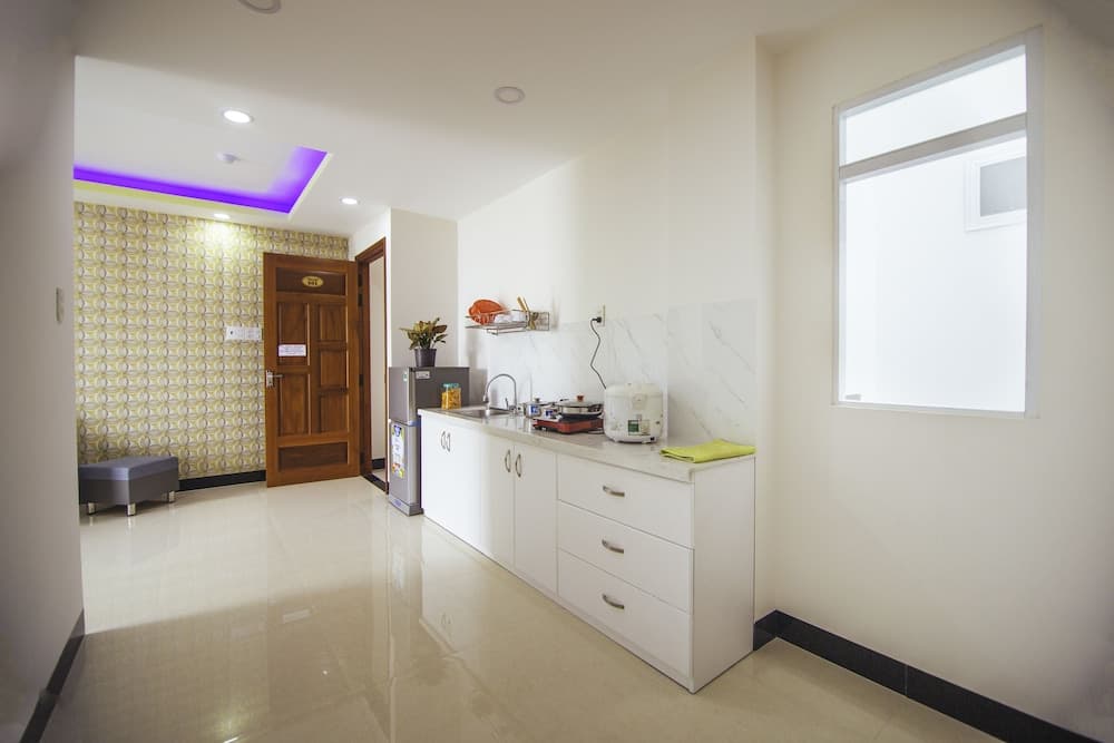 A modern kitchenette with white cabinetry, a rice cooker, and a window, adjacent to a hallway with a patterned wall and wooden door, ideal for travelers seeking self-catering accommodations in an urban setting.