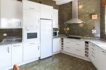 A modern kitchen with sleek white cabinets, stainless steel appliances, and green tiled walls exudes a clean and functional atmosphere, ideal for travelers seeking a cozy self-catering accommodation.