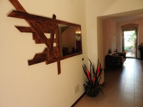 A cozy indoor hallway features a rustic wooden-framed mirror reflecting warm lighting, vibrant potted plants adding a touch of nature, and an inviting open doorway leading to a sunlit patio, perfect for travelers seeking a charming and serene accommodation experience.