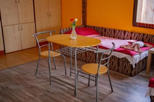 A cozy guesthouse room features a vibrant orange wall, wooden flooring, a small dining table with chairs, and neatly arranged beds, creating a welcoming atmosphere ideal for budget travelers seeking comfort.