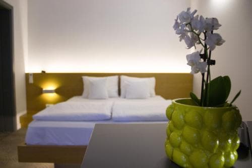 A cozy hotel room features a neatly made bed with soft lighting, a vibrant green vase holding white orchids on the table, creating a serene and inviting atmosphere ideal for travelers seeking relaxation.