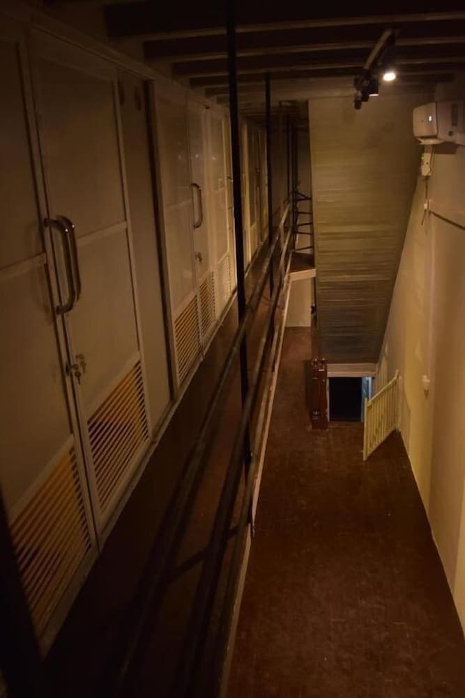 A dimly lit hostel corridor with wooden floors, metal railings, and rows of lockers creates an intimate and cozy atmosphere ideal for budget travelers seeking a unique accommodation experience.