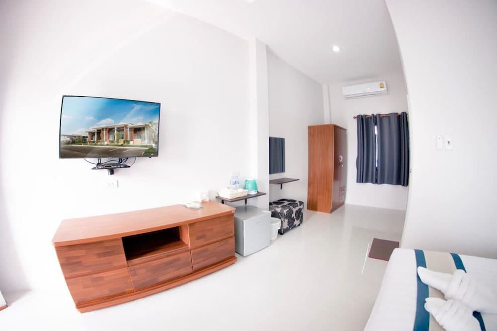 A cozy hotel room features a sleek wooden TV stand, mounted flat-screen displaying a serene outdoor scene, a mini-fridge, and neatly arranged bedding, ideal for travelers seeking comfort and simplicity.