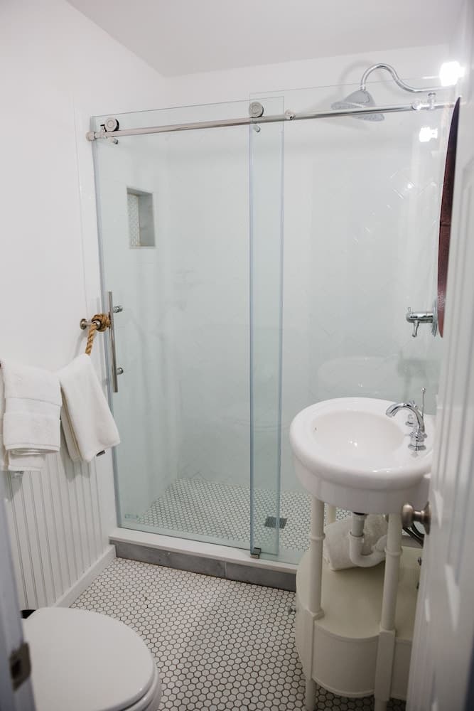 A cozy, modern bathroom features a glass-enclosed shower with hexagonal tiles, a sleek white pedestal sink, and a toilet, ideal for travelers seeking compact yet stylish accommodations.
