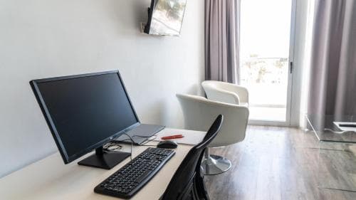 A cozy hotel room workspace features a sleek desk setup with a computer, modern chairs, and a balcony view, ideal for travelers seeking productivity and relaxation.