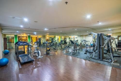 A well-lit indoor gym with polished wooden floors, various exercise machines, and mirrors creates an inviting atmosphere for travelers seeking fitness facilities during their stay.