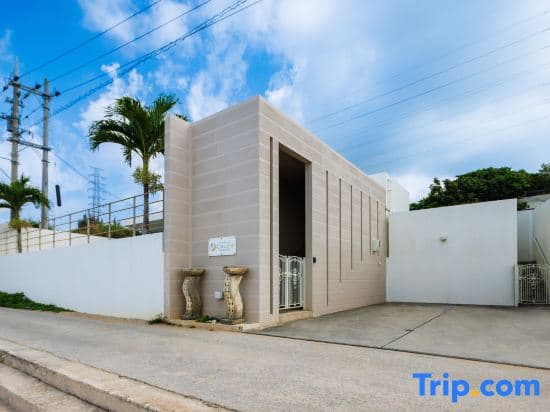 A serene tropical villa entrance with palm trees and clear skies offers a tranquil getaway, ideal for travelers seeking relaxation and modern amenities.