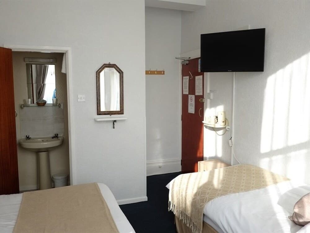 A cozy hotel room with two neatly made beds, a mounted TV, a small sink area, and soft sunlight filtering through the window, ideal for budget travelers seeking comfort and simplicity.